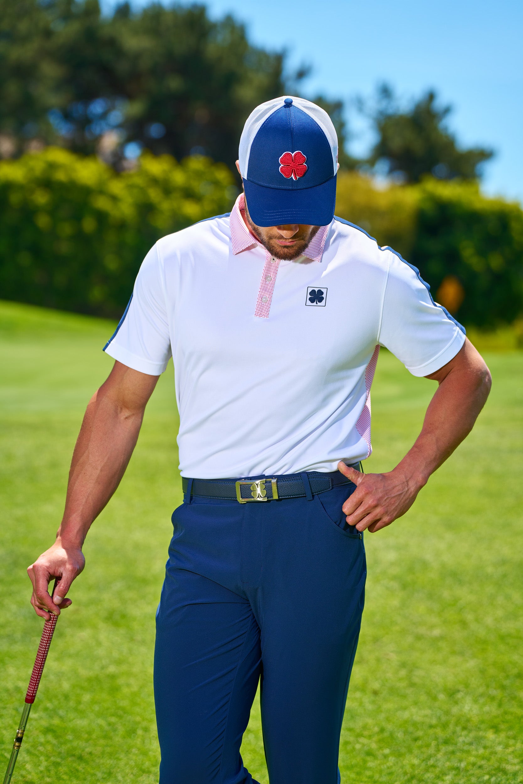 Man standing at golf course in blue Black Clover Live Lucky hat.