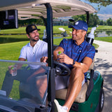 Two men sitting in a golf car wearing Black Clover Live Lucky Apparel and Hats.