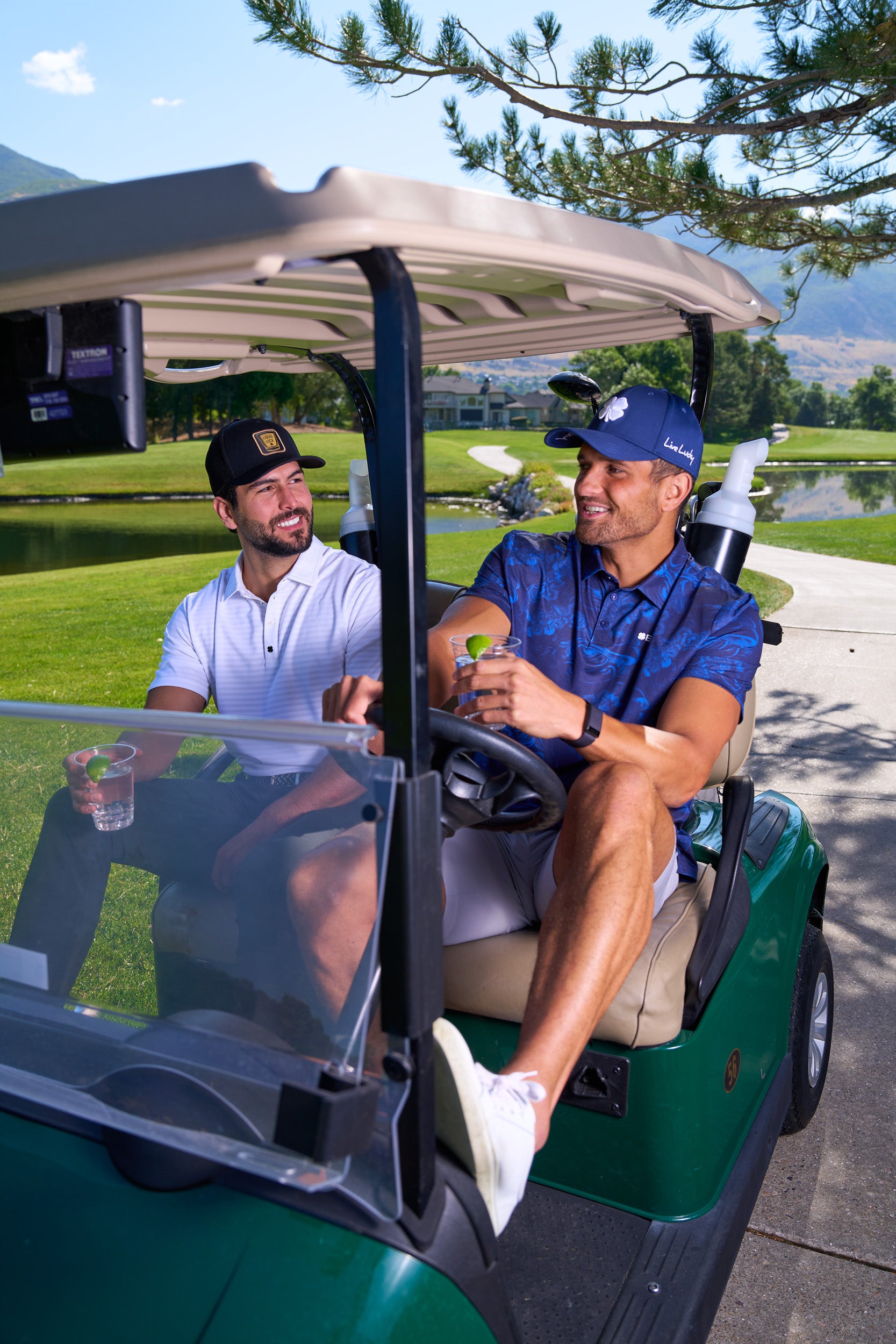 Two men sitting in a golf car wearing Black Clover Live Lucky Apparel and Hats.