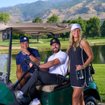 Two men in a golf cart with a woman standing next to them, all of whom are wearing Black Clover Live Lucky apparel. 