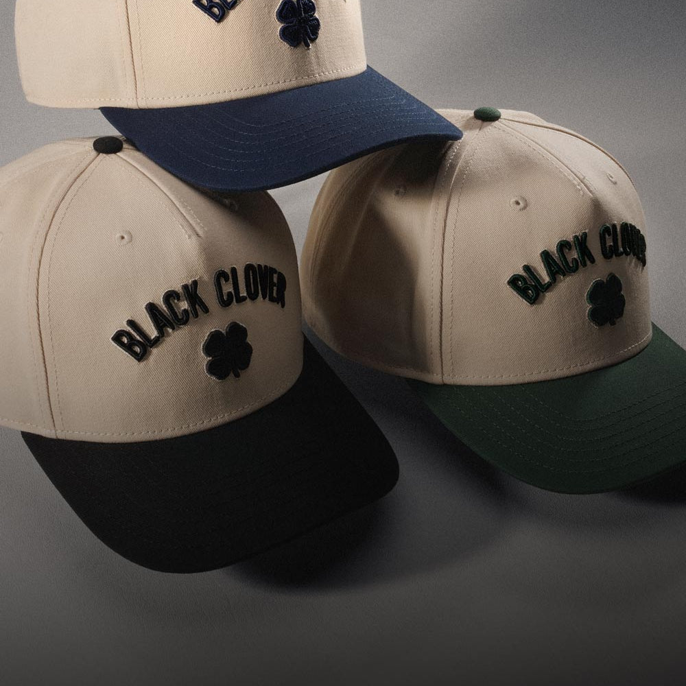 Stacked timeless Black Clover Live Lucky hats in studio on grey background.