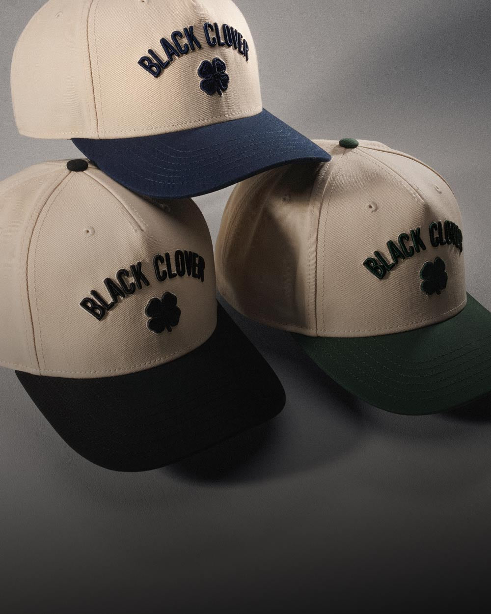 Stacked timeless Black Clover Live Lucky hats in studio on grey background.
