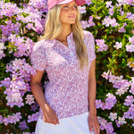 Woman standing next to pink flowers wearing Black Clover Live Lucky premium clover hat in pink and black.
