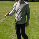 Man wearing grey Black Clover Live Lucky apparel at the golf course holding a club over his shoulder. 