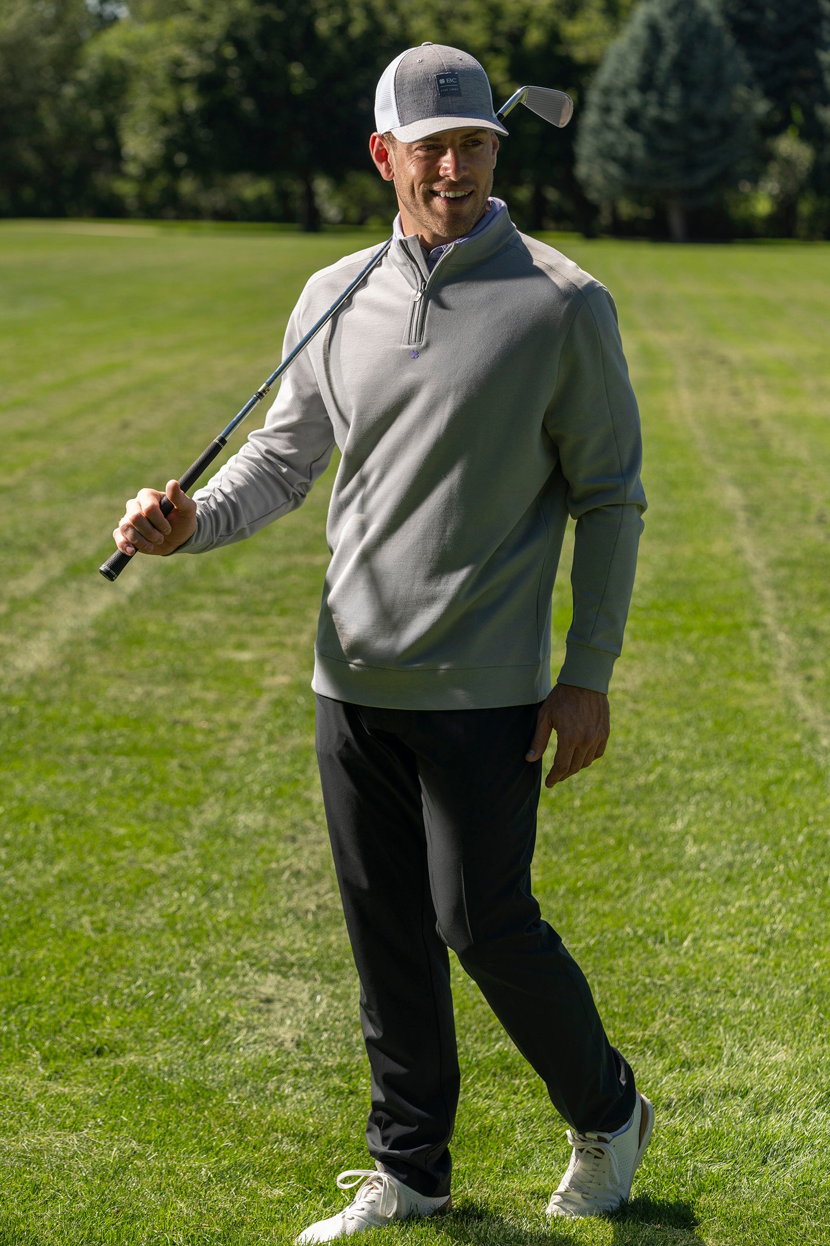 Man wearing grey Black Clover Live Lucky apparel at the golf course holding a club over his shoulder. 