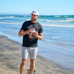 Man holding american football at the beach wearing CLVR Black Clover Live Lucky hat.