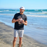 Man holding american football at the beach wearing CLVR Black Clover Live Lucky hat.