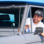 Man leaning out the window of his car wearing a Black Clover Live Lucky CLVR hat in white.