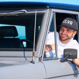 Man leaning out the window of his car wearing a Black Clover Live Lucky CLVR hat in white.